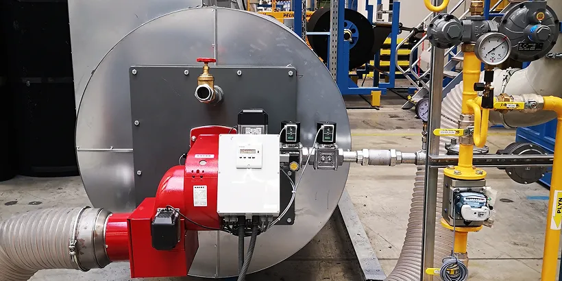 Industrieller Kessel mit rotem Brenner und gelben Rohren in einer Fabrikumgebung.