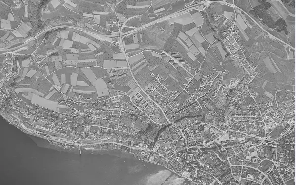 Schwarz-weiß-Luftaufnahme einer Stadt mit Fluss, Straßen, Gebäuden und landwirtschaftlichen Flächen.