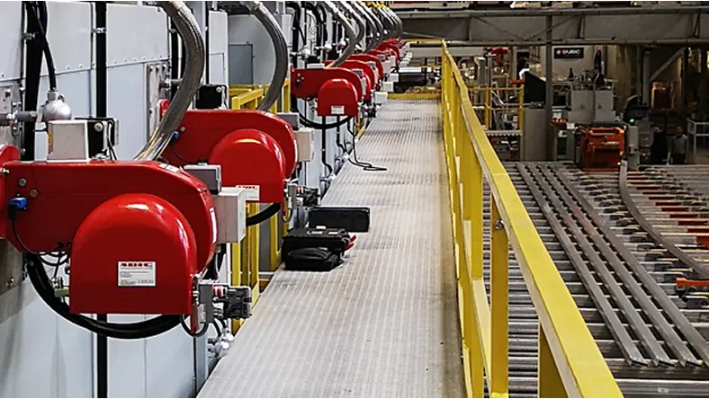 Industrielle Maschinen mit roten Gehäusen entlang eines Laufstegs mit gelben Geländern.