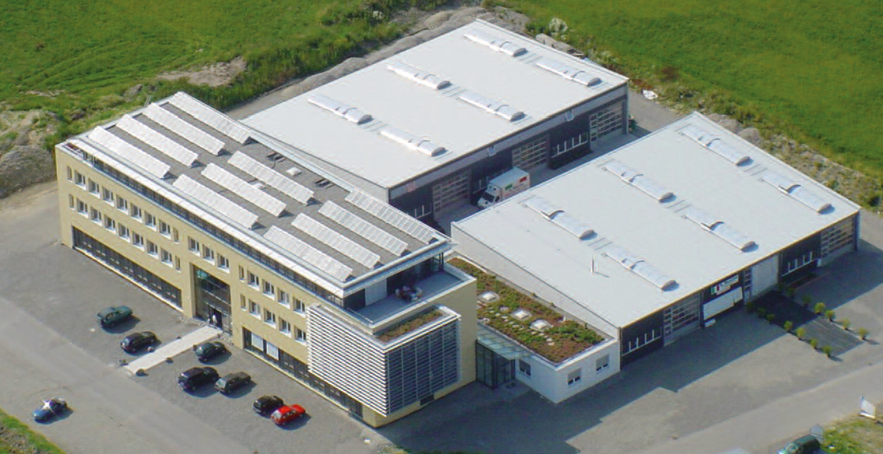 Luftaufnahme eines Büro- und Lagergebäudes mit Solarpaneelen und Begrünung auf dem Dach.