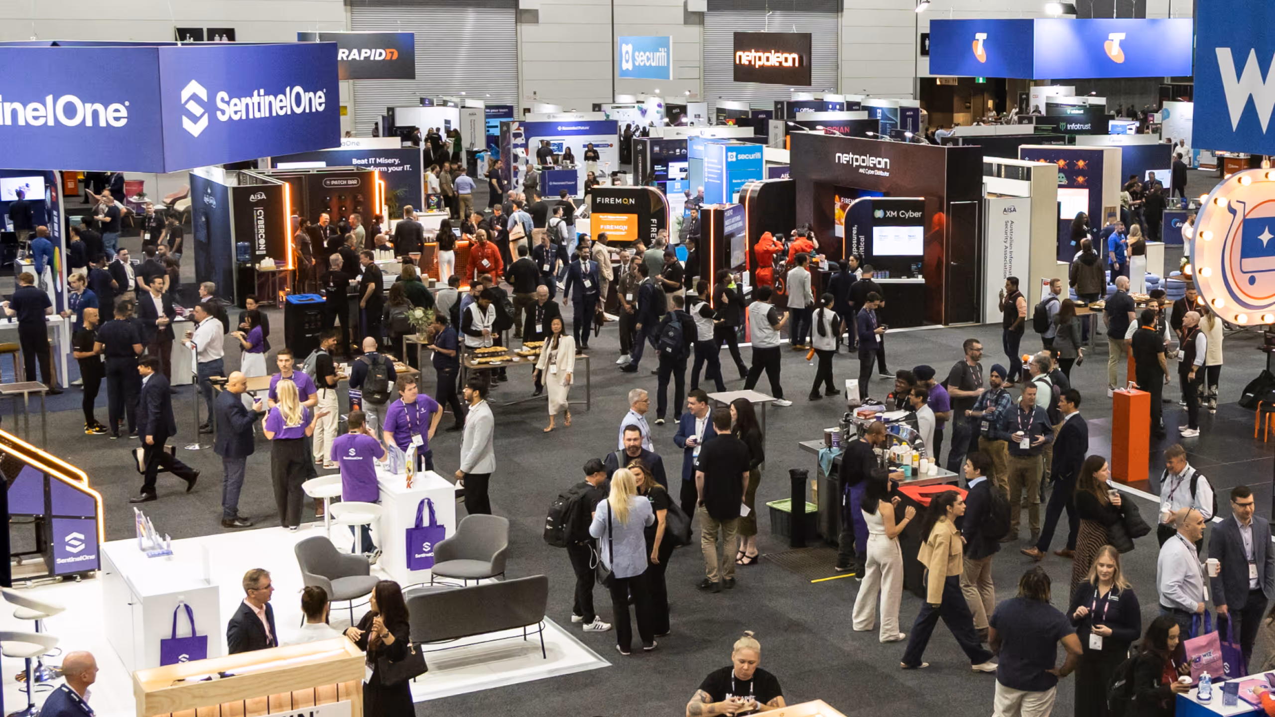 Busy technology expo floor with people networking and company booths featuring SentinelOne and others.