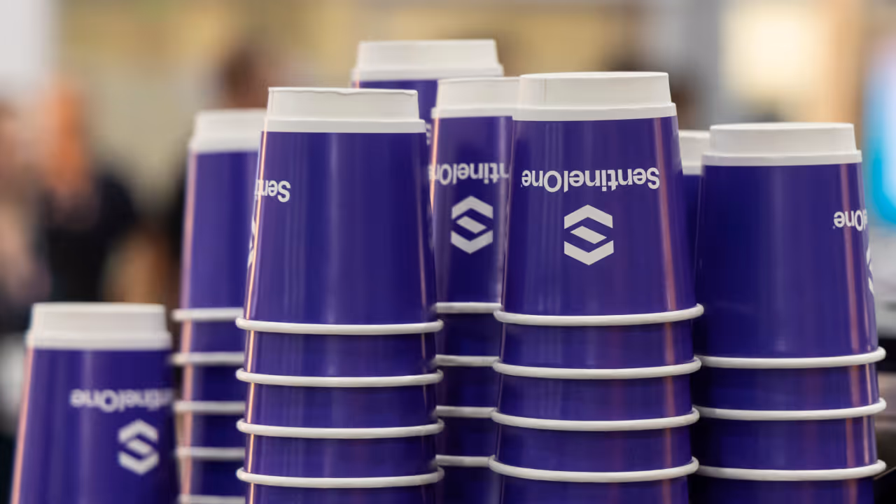 Stacks of purple cups with white lids displaying a logo and text on a blurred background.