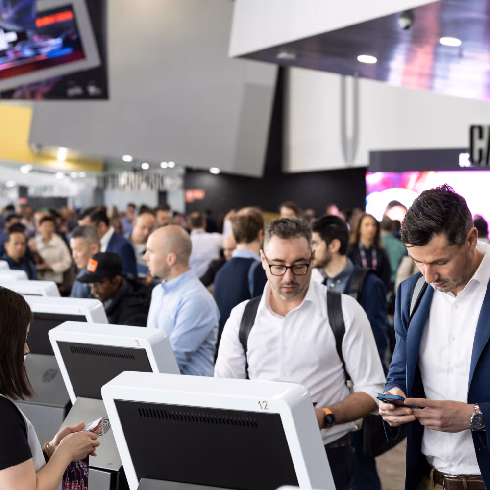 Crowd of people at check-in kiosks in a busy airport or event venue lobby.
