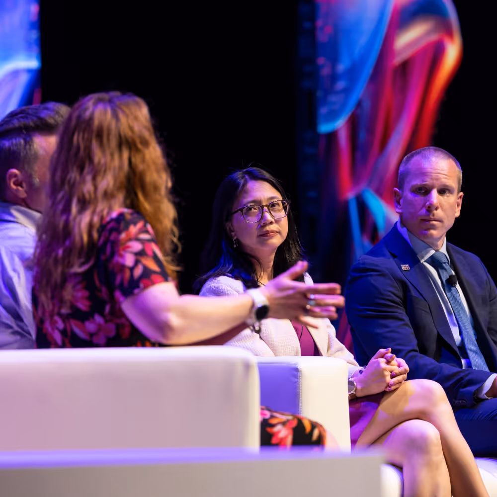 Four people seated on stage engaged in a panel discussion with a dark colorful background.