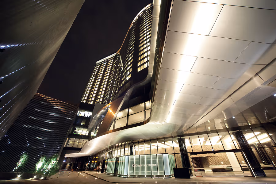 Modern high-rise building with curved glass facade and bright lights at night.