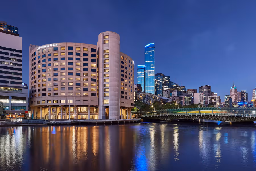 Crowne Plaza hotel building and city skyline reflected in calm river water at dusk in Melbourne.