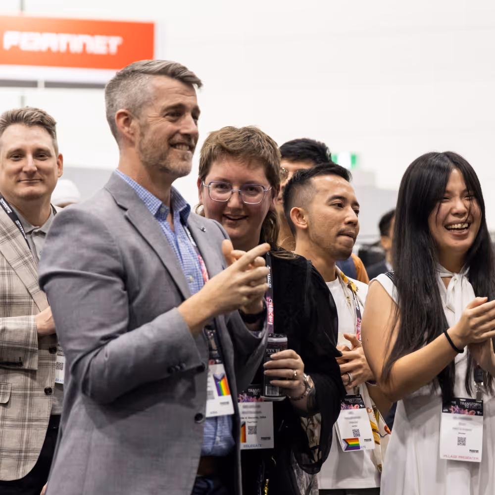 Group of diverse people at an event, smiling and clapping with badges and lanyards.