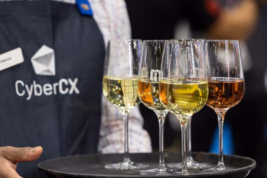 Server in a CyberCX apron carrying a tray of wine at CyberCon
