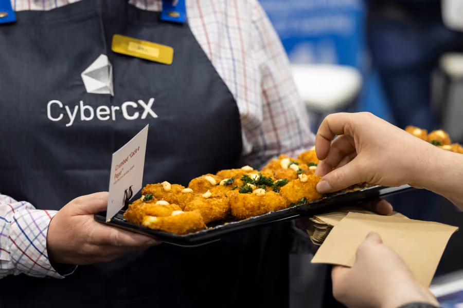 Server in a CyberCX apron offering a tray of canapes at CyberCon