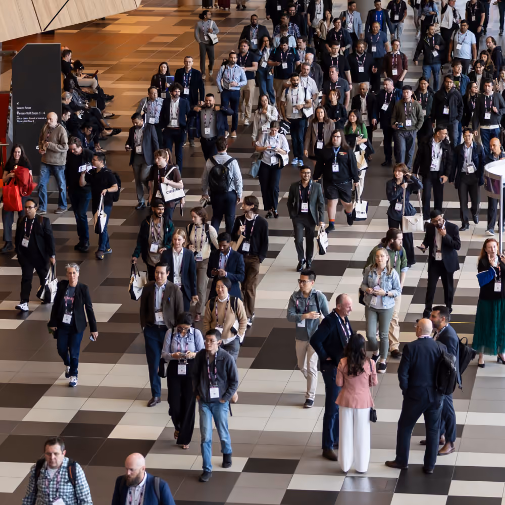 Crowd of diverse people walking inside a spacious convention center with patterned floor tiles.