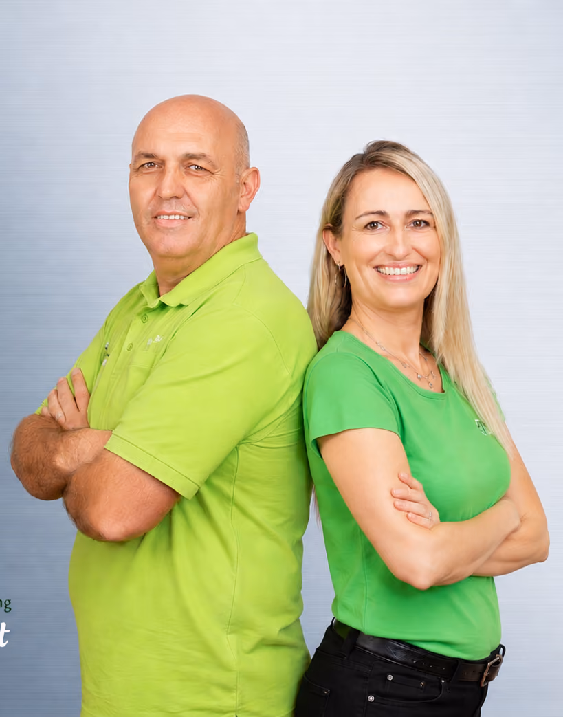 Man and woman in green shirts standing back to back with arms crossed smiling at the camera.