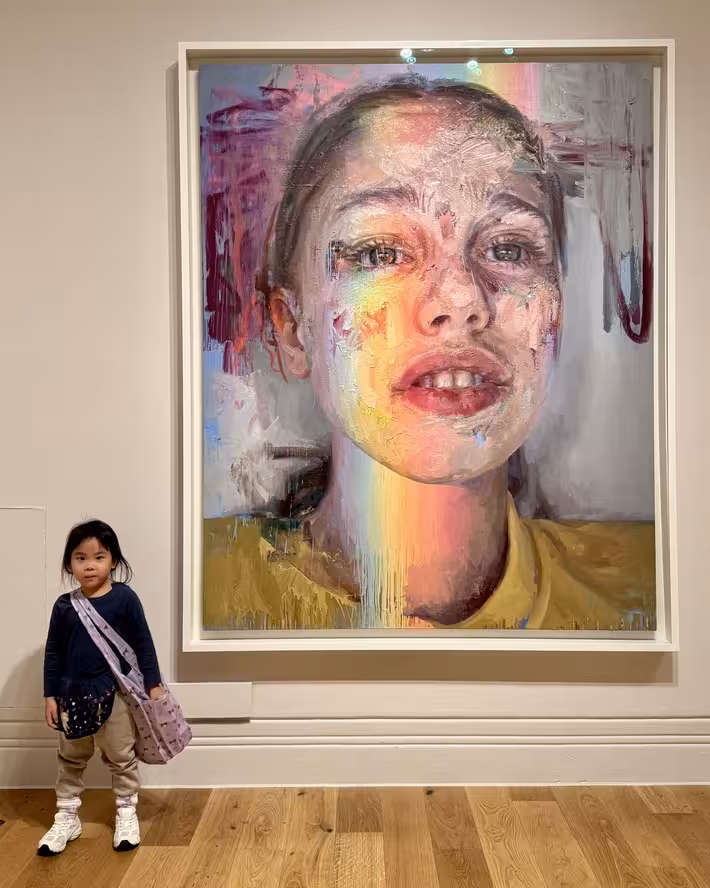 Young child looking up at a large Jenny Saville portrait painting in a gallery