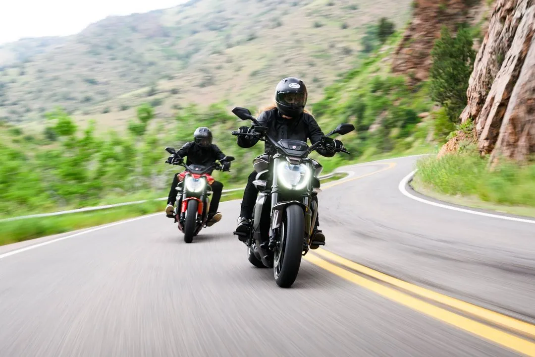 Zwei Motorradfahrer auf Ducati-Maschinen fahren eine kurvige Bergstraße entlang.