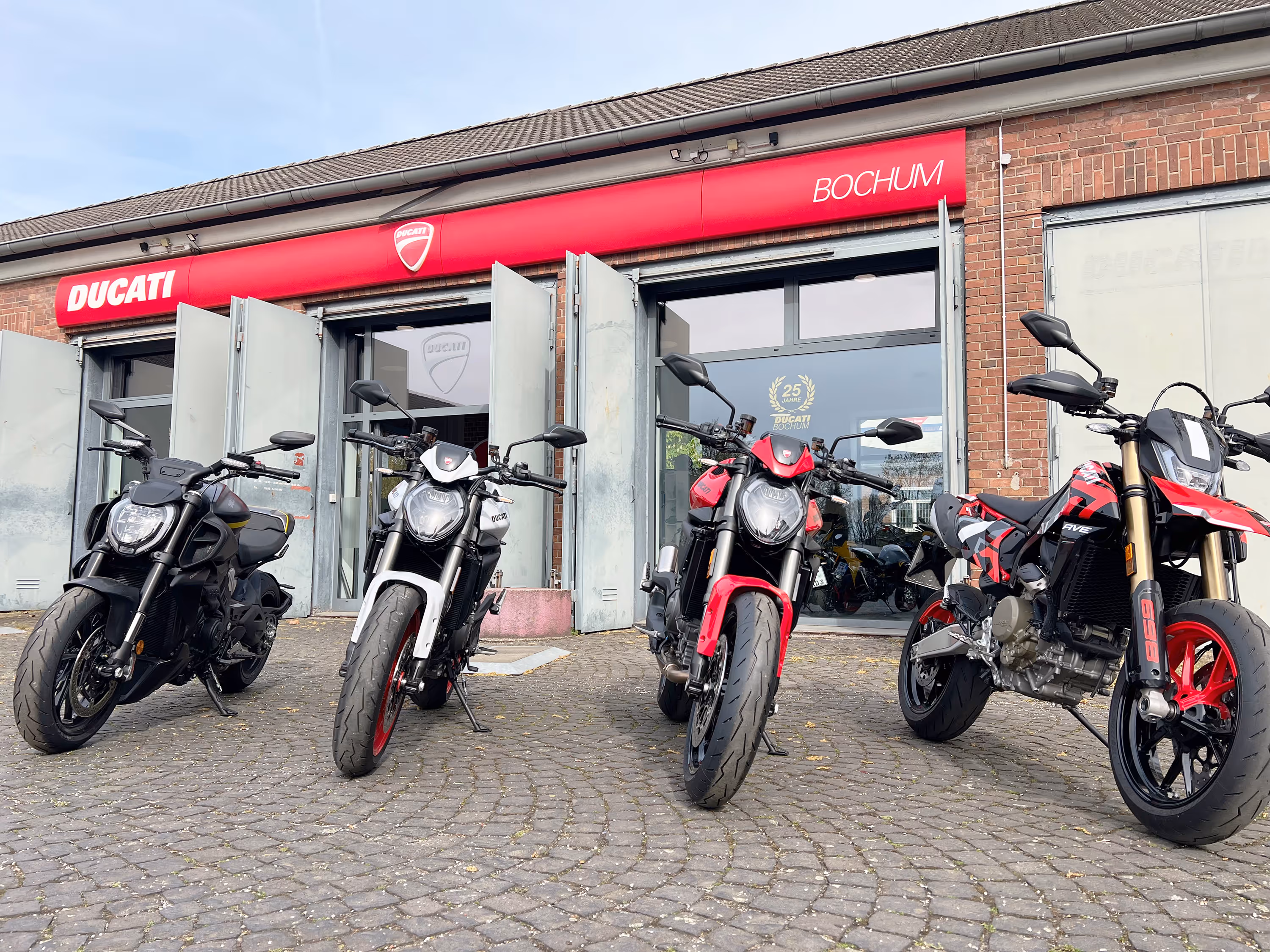 Zwei Ducati-Motorräder, ein gelbes Sportmodell und ein schwarzes Scrambler-Modell, vor einem Ducati-Händler mit roten Logos.