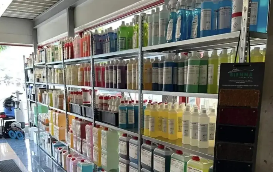 Shelves stocked with various cleaning or chemical bottles in different colors and sizes in a brightly lit storage room.