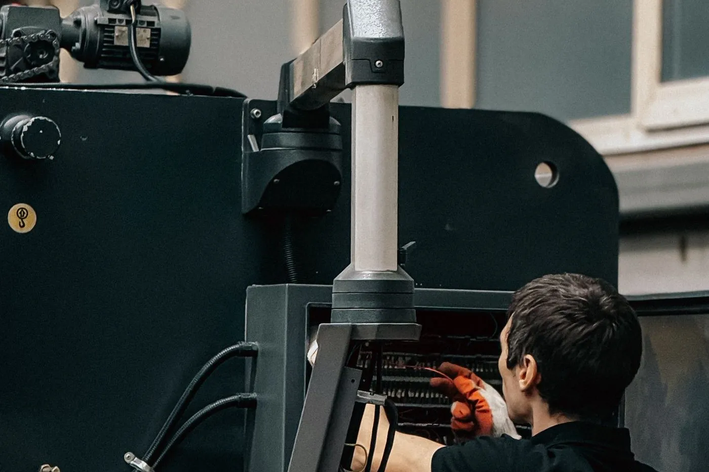 Technician in work gloves reaching into an open machine control cabinet