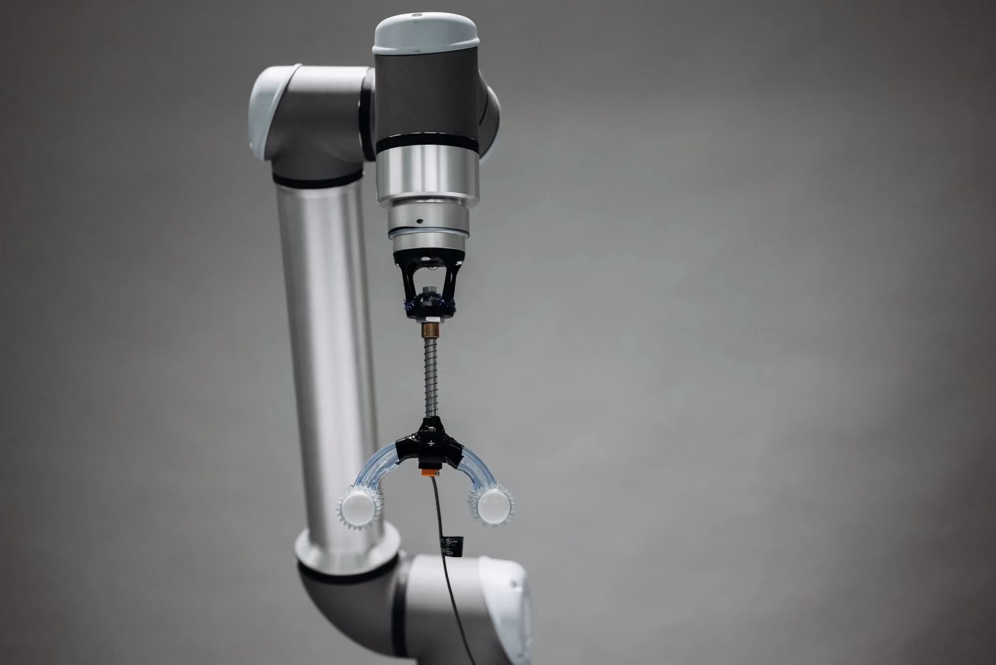 Collaborative robot arm fitted with a two-finger gripper against a pale background