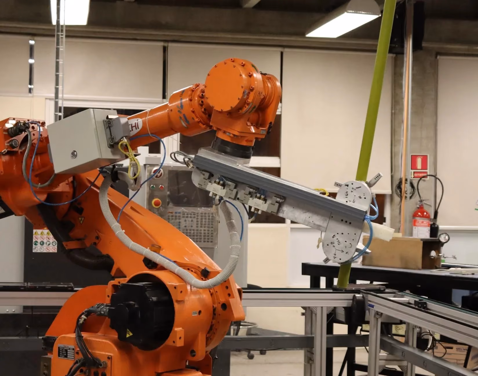 Six-axis industrial robot arm carrying a vacuum end-effector inside an aluminium-framed cell