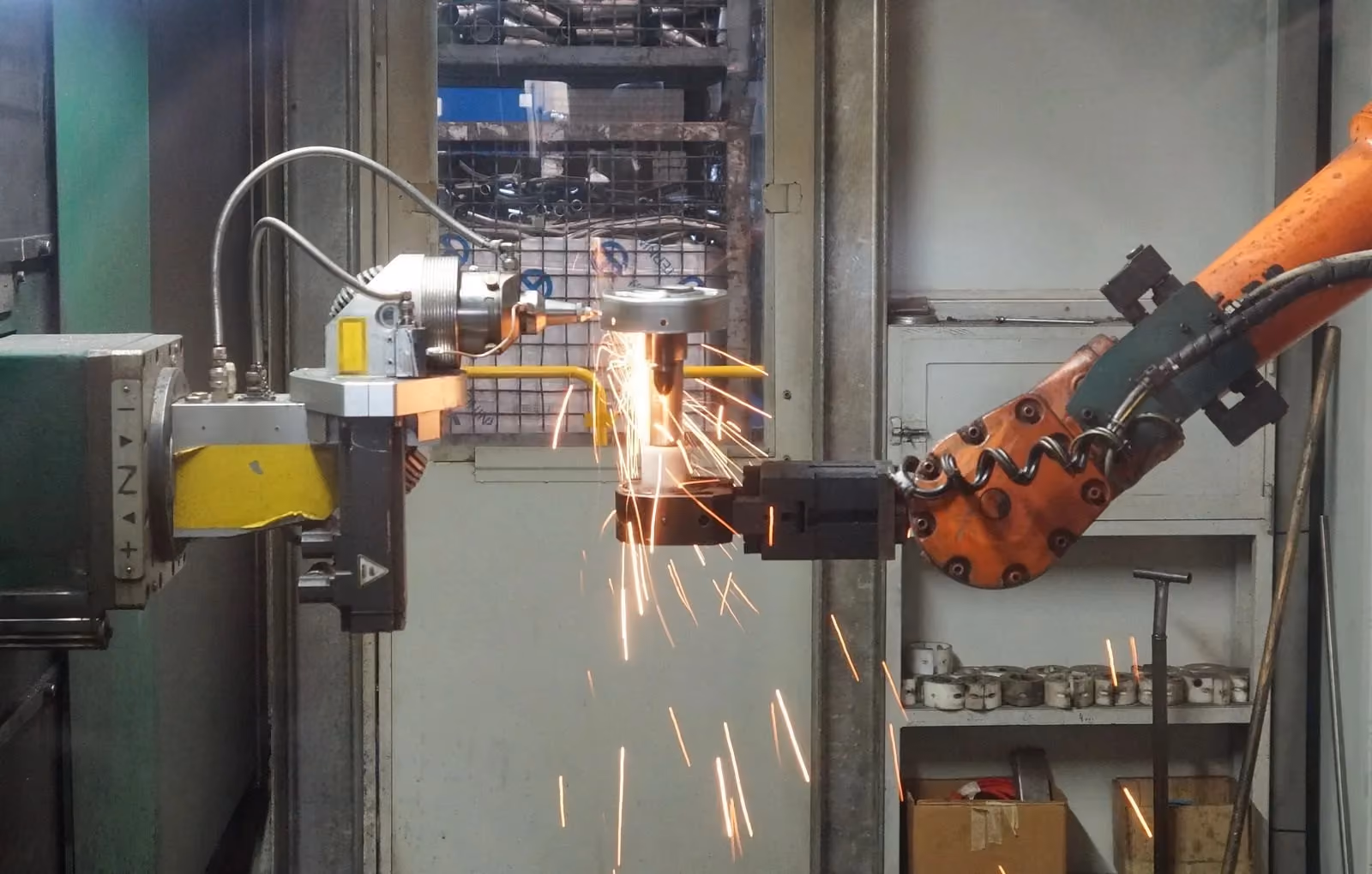 Robot arm working a part inside a guarded station, sparks falling below the tooling