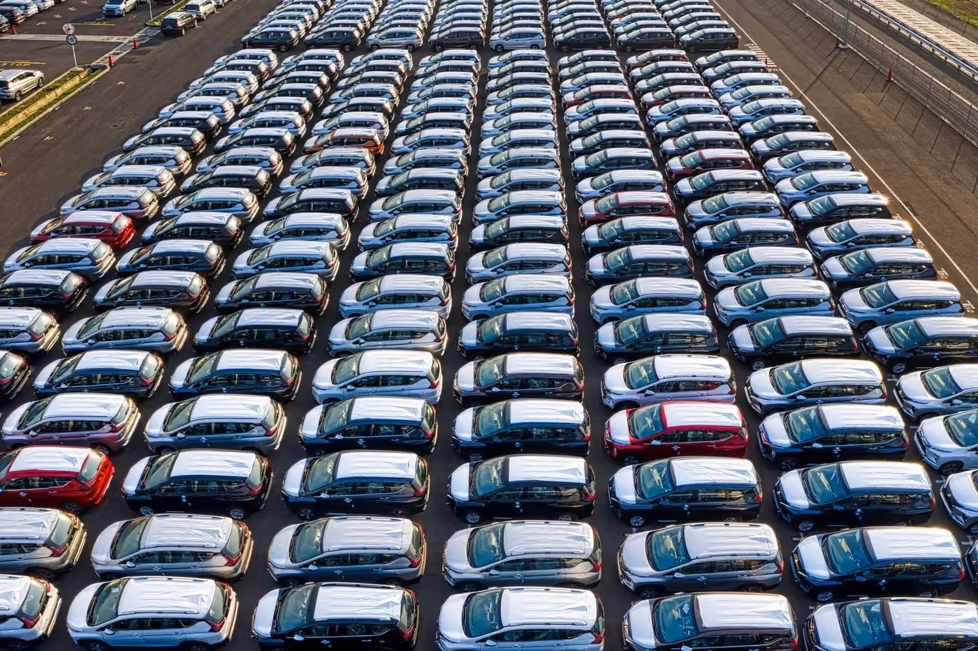 Rows of finished vehicles in a marshalling yard beside a plant