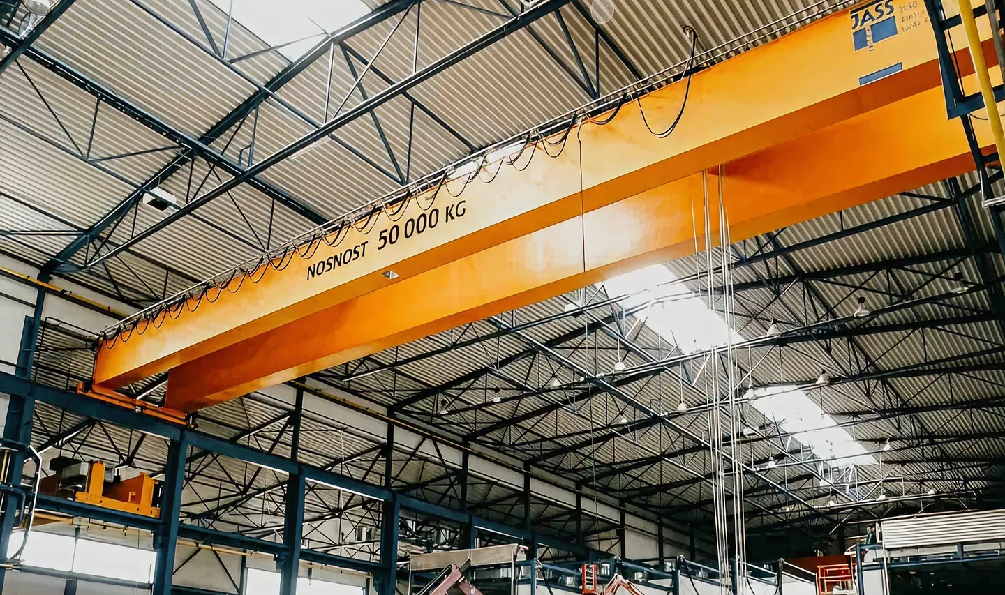 Velký oranžový jeřáb s nápisem nosnost 50 000 kg v průmyslové hale s kovovou konstrukcí.