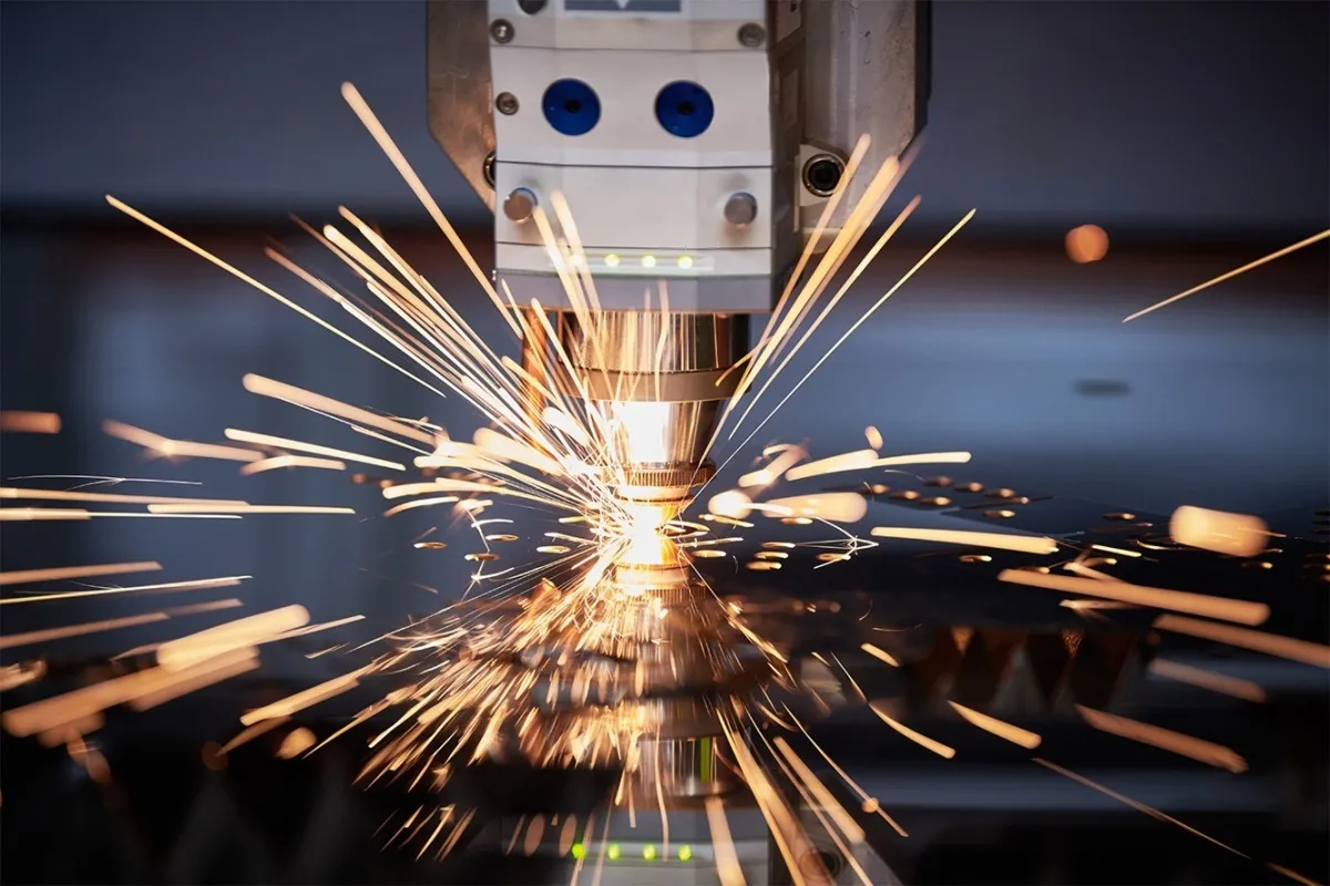 Průmyslový laser vypalující kovové materiály s jiskrami v dílně.