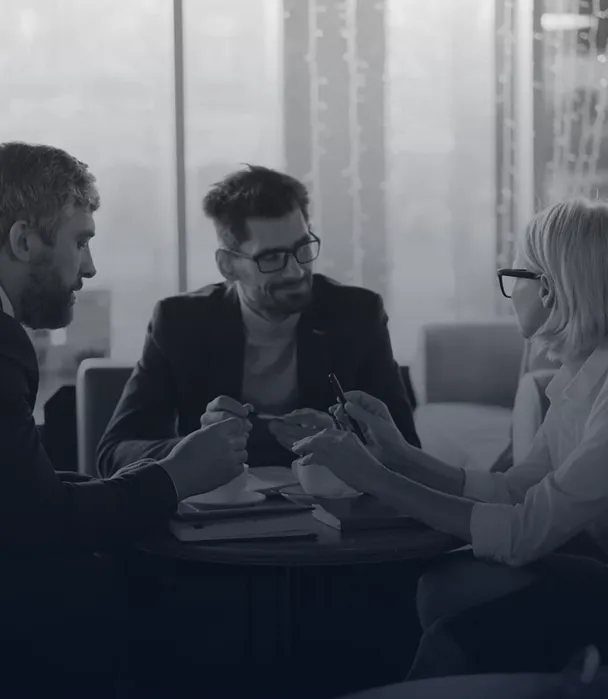 Three professionals wearing glasses engaged in discussion around a round table in a modern office setting.