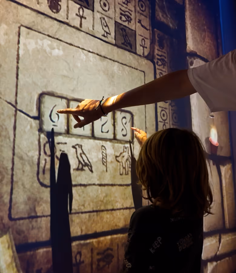 Deux joueurs touchent une paroi couverte de hiéroglyphes pour résoudre une énigme