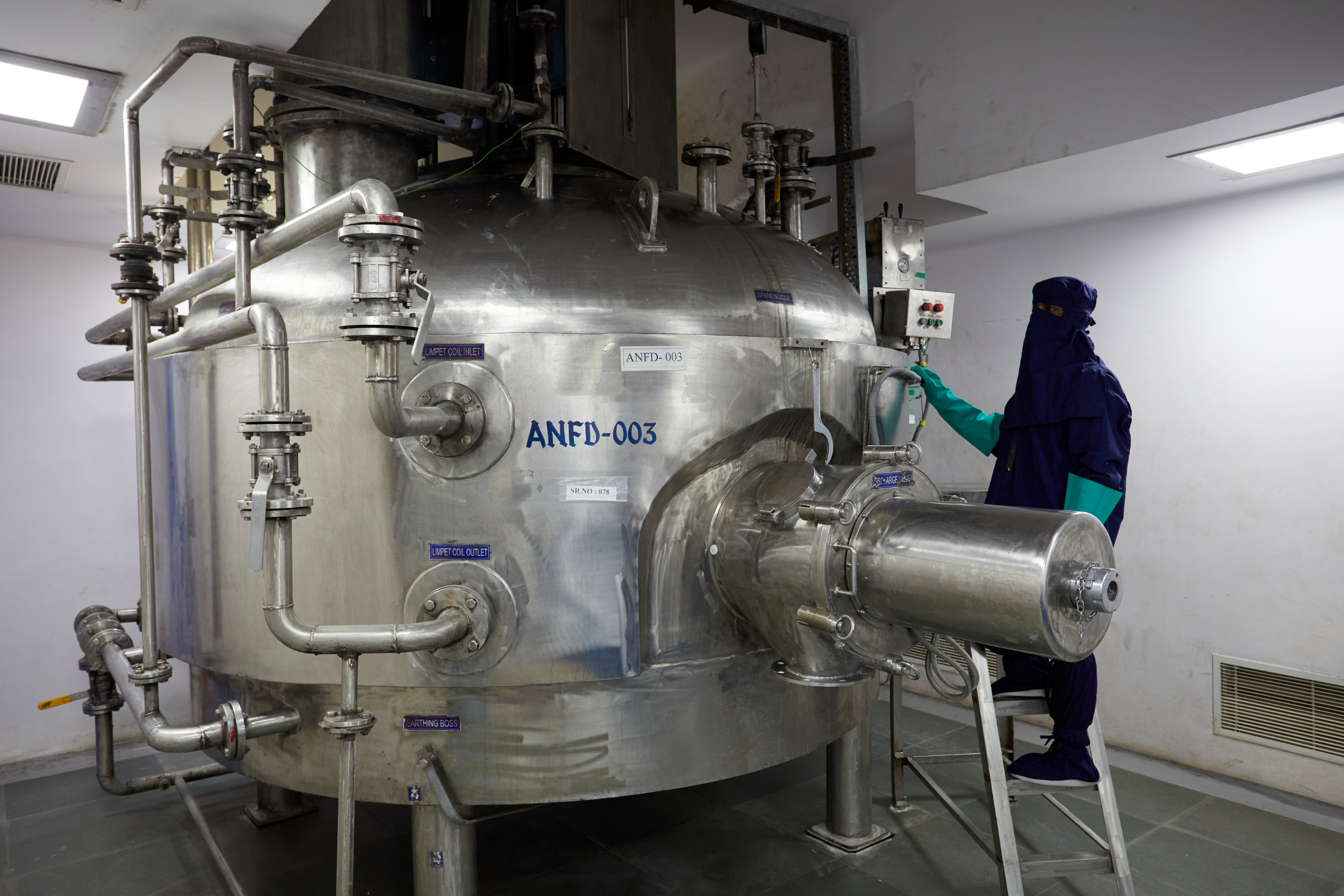 Technician operating a stainless steel Agitated Nutsche Filter Dryer (ANFD) in a GMP-compliant chemical manufacturing facility.
