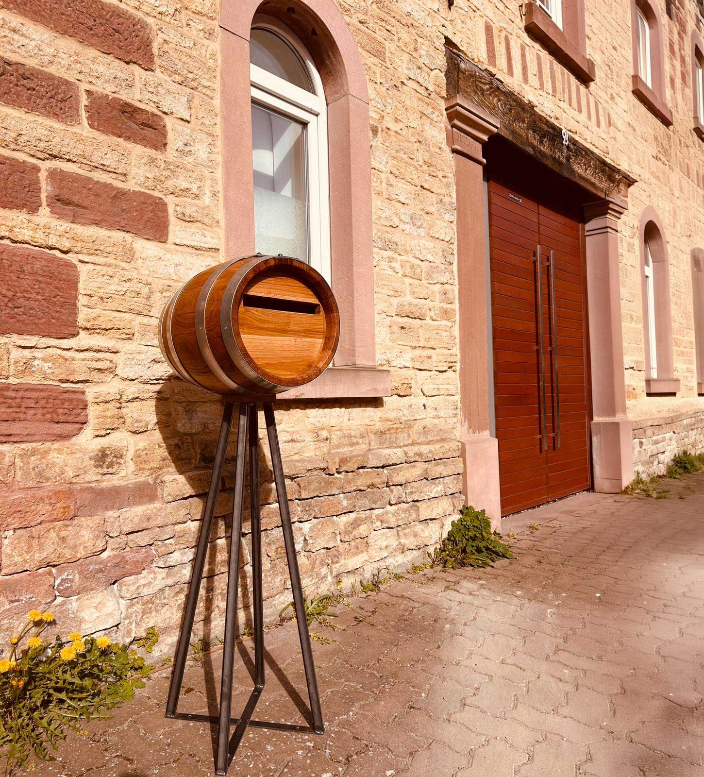 Barrikat-Postfass auf einem Stahlgestell vor einem historischen Steingebäude in der Pfalz