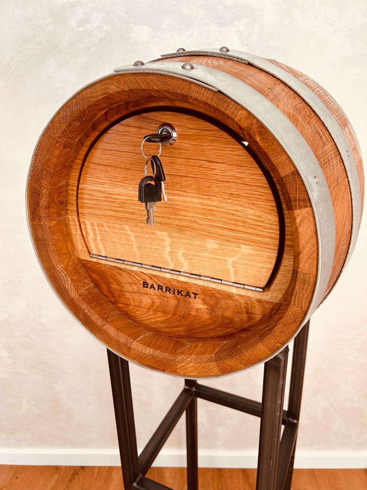 Wooden barrel with metal bands and keys in lock on a black metal stand.