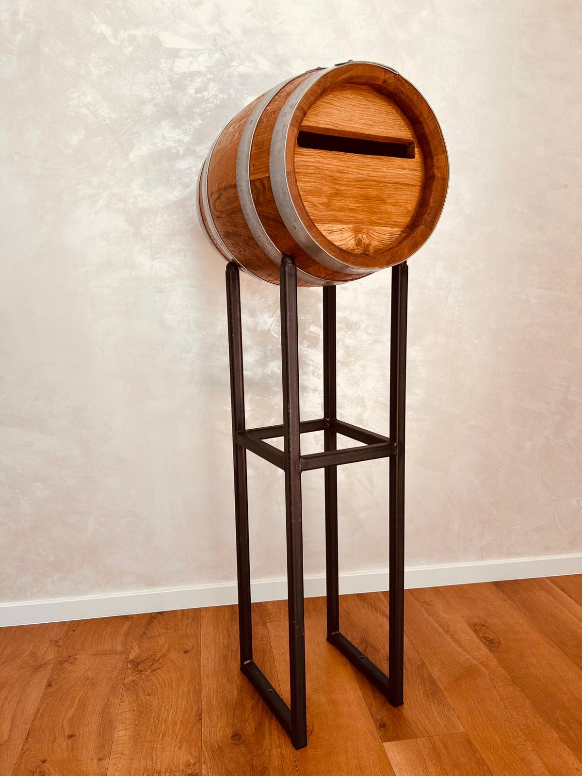 Wooden barrel with metal bands on a tall black metal stand against a beige wall and hardwood floor.