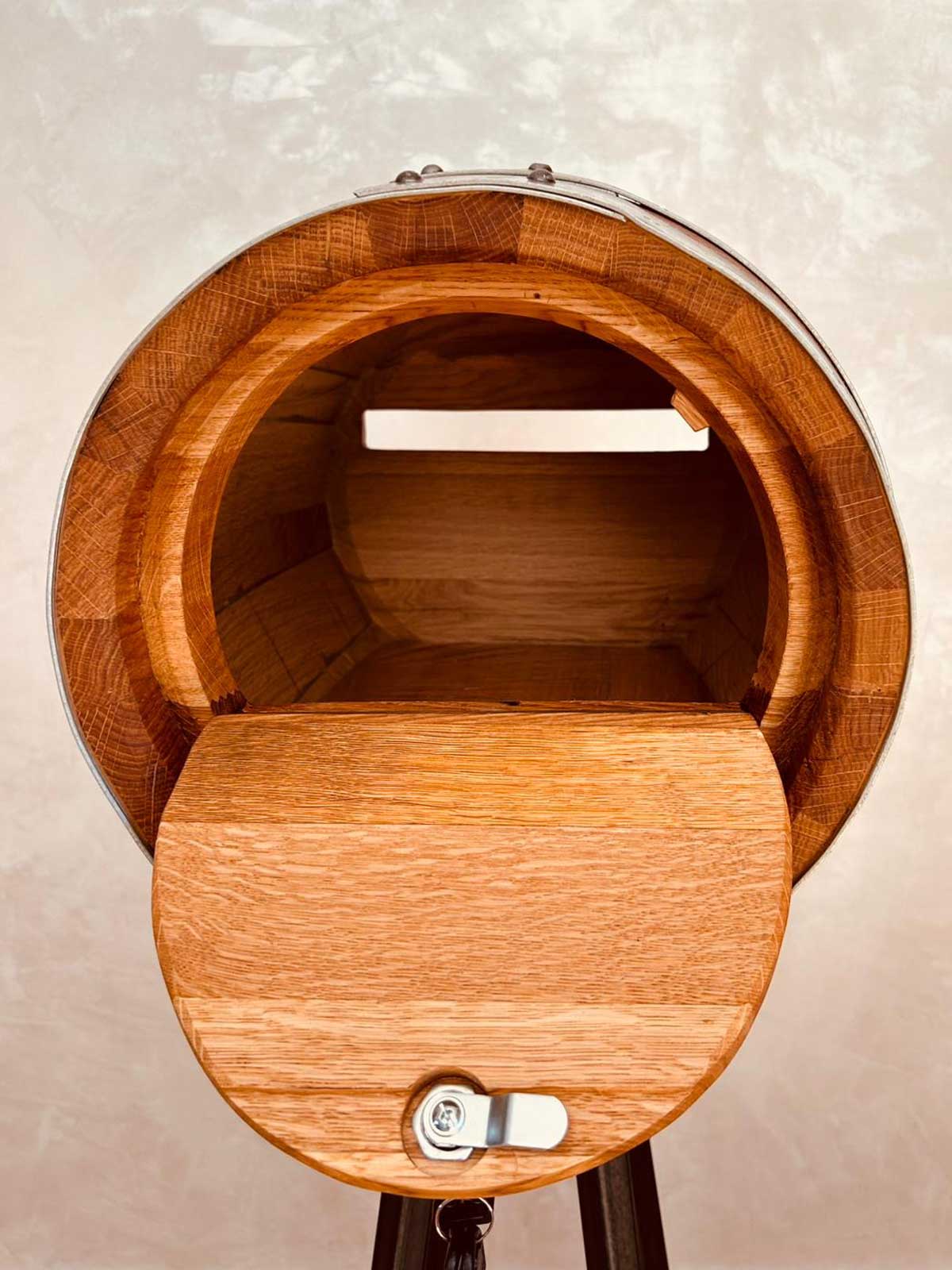 Open round wooden mailbox with metal latch and a slot inside, mounted on a tripod stand.