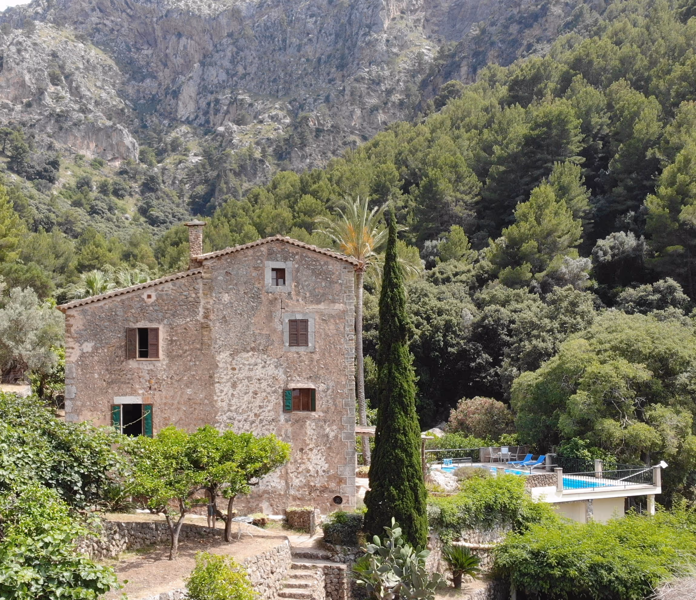 Traditional stone house with a tall cypress and mountain backdrop, overlooking the pool at Finca Higo.