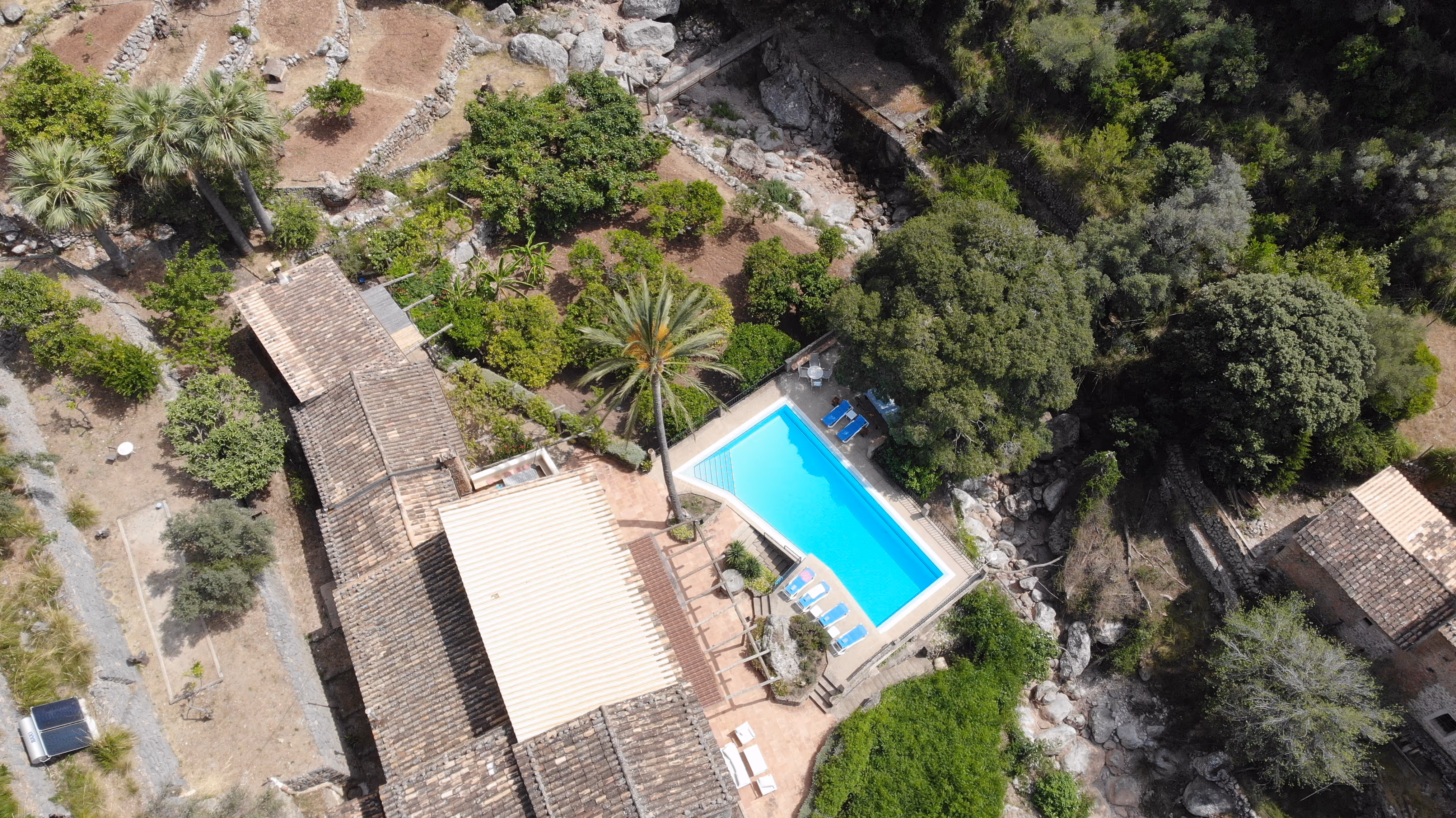 Aerial view of Finca Higo’s pool area surrounded by stone buildings, palm trees, and rocky landscape.