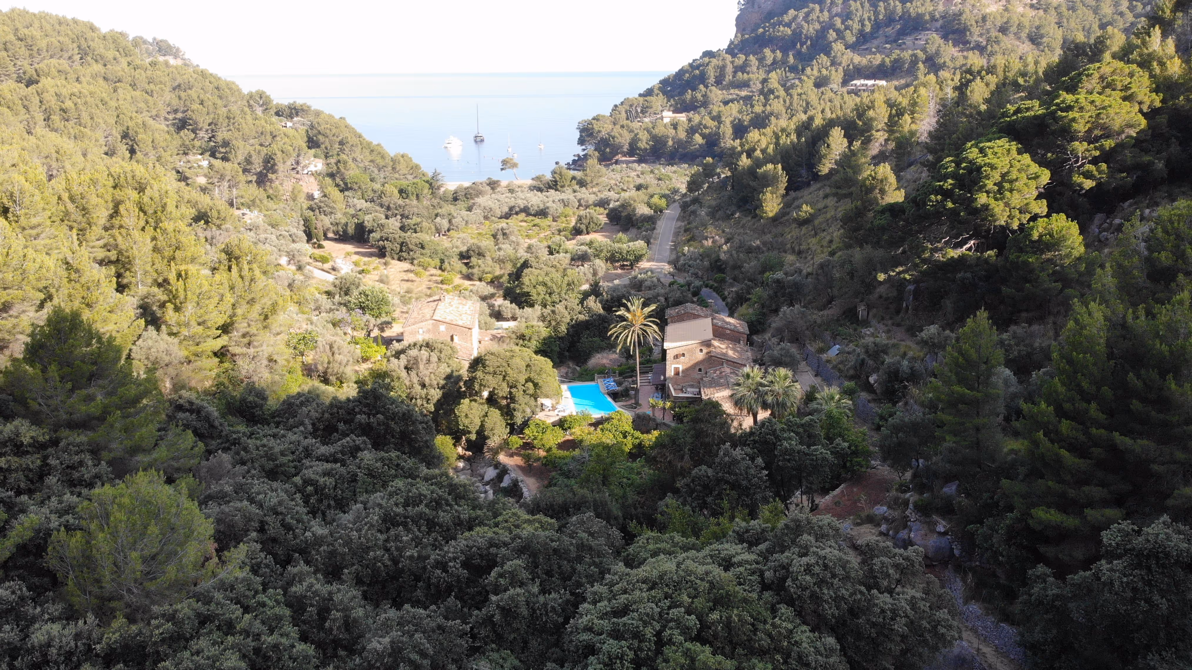 Drone view of Finca Higo retreat surrounded by trees, with the turquoise sea and moored boats in the distance.