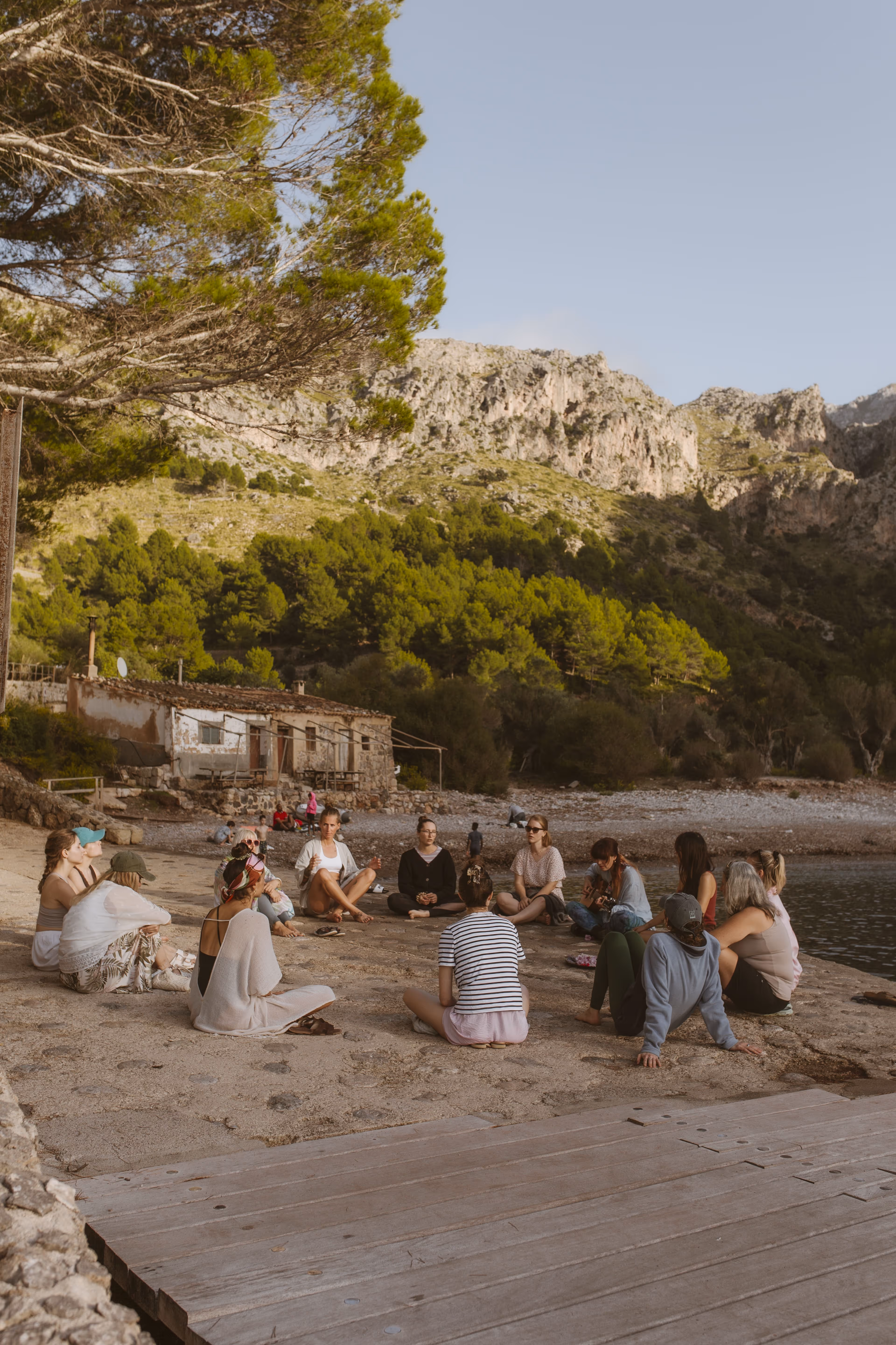 People sitting in a meditation circle on the beach of Cala Tuent, practicing yoga in Mallorca.