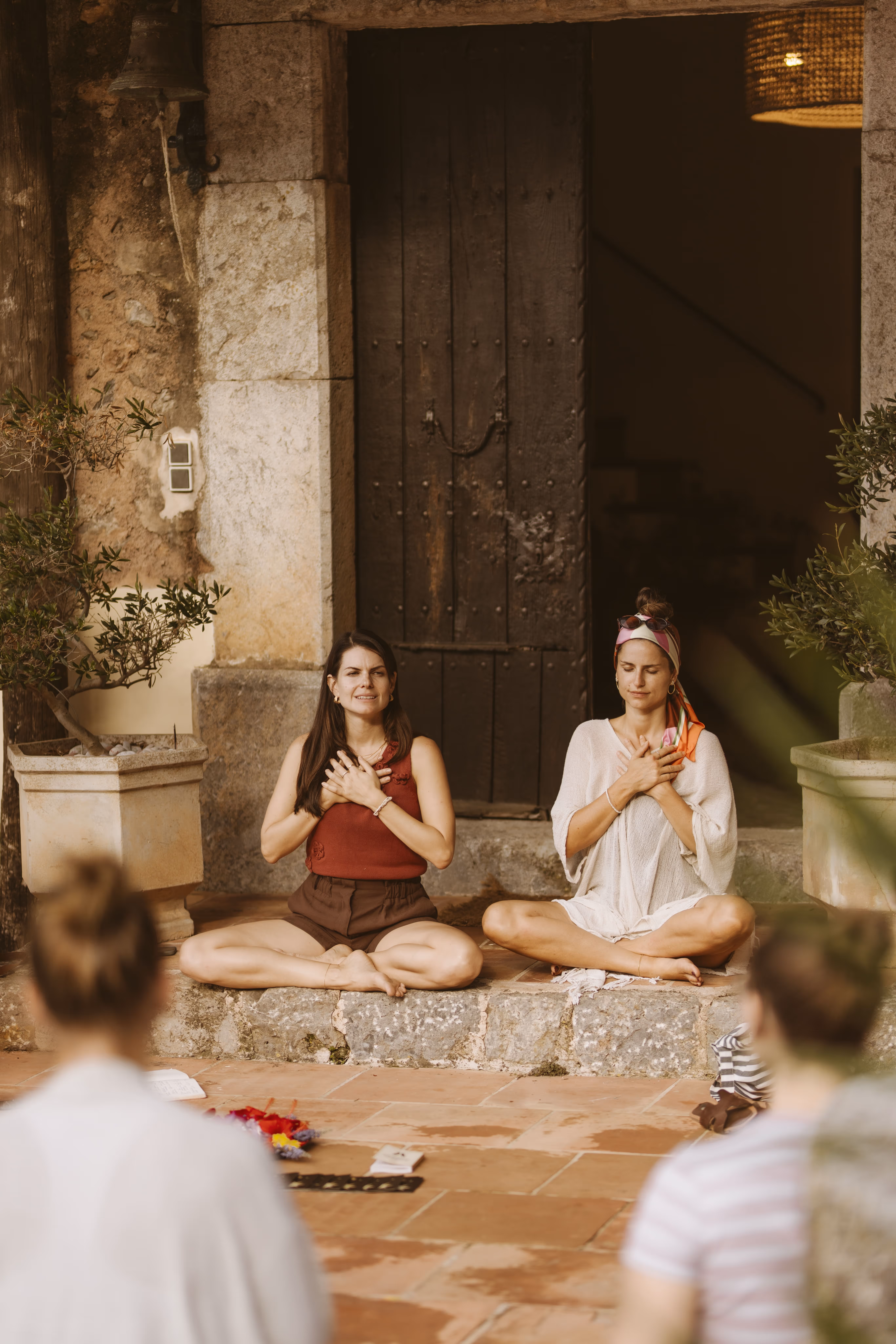 Two female yoga teachers meditating in front of the main door of Finca Higo’s historic walls.