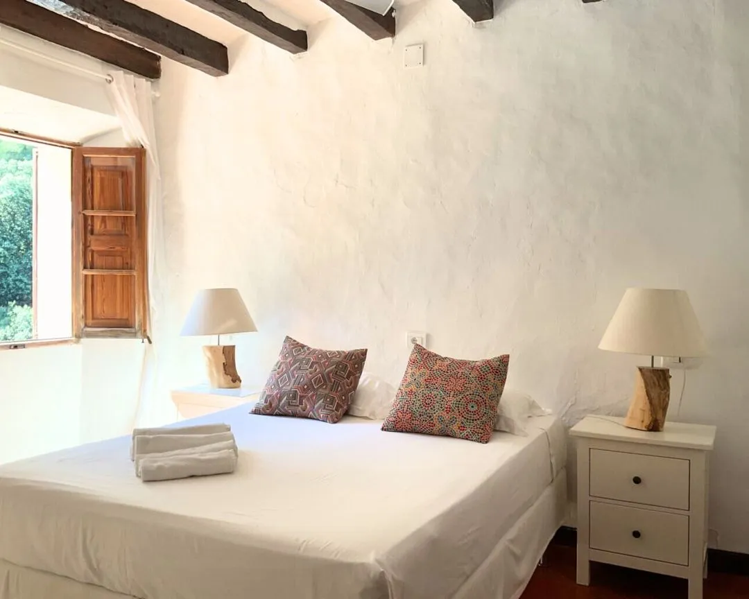 Bright bedroom with white rustic walls, a double bed, and two authentic wooden bedside tables with lamps.