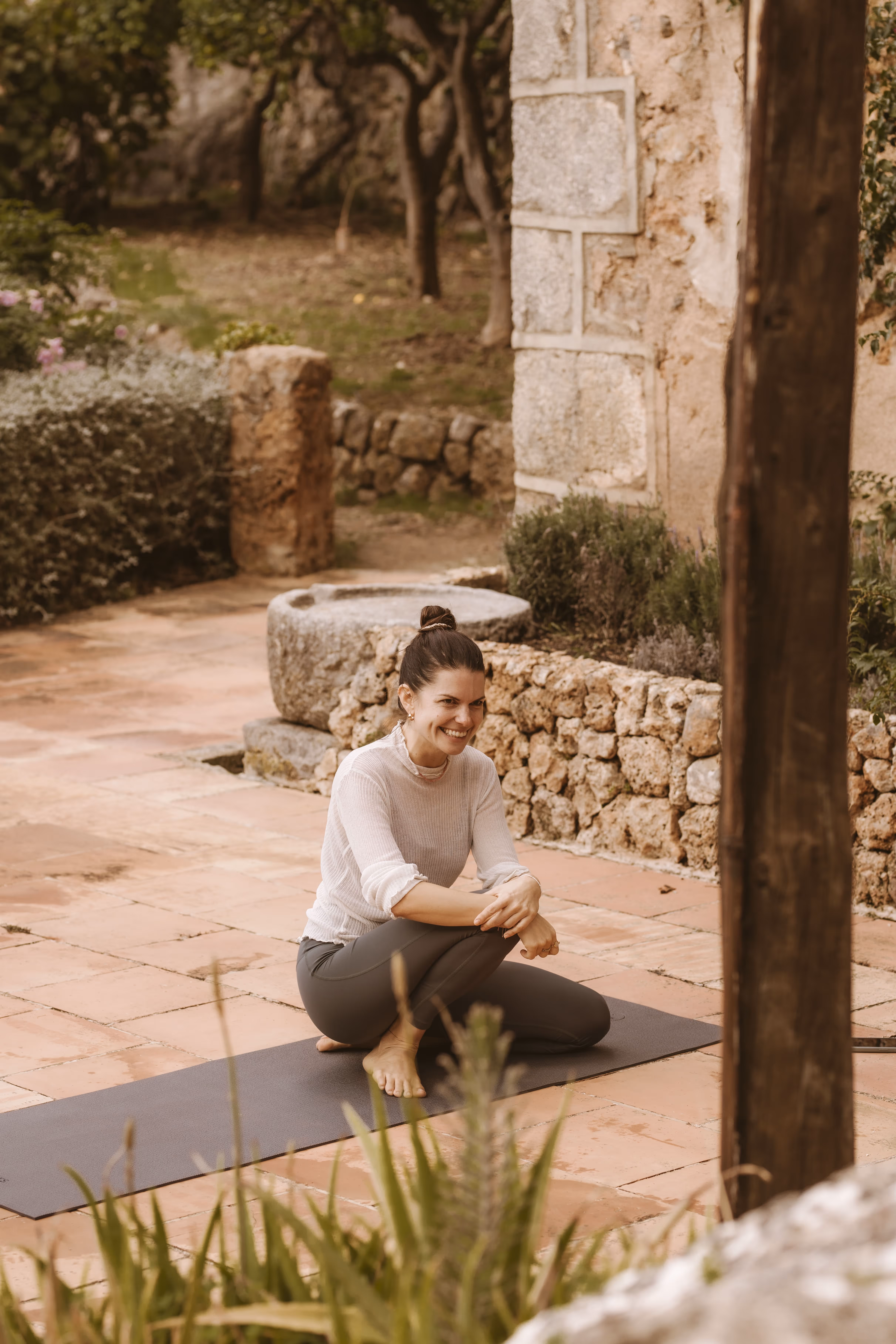Yoga teacher sitting on a yoga mat outdoors, smiling during a session.