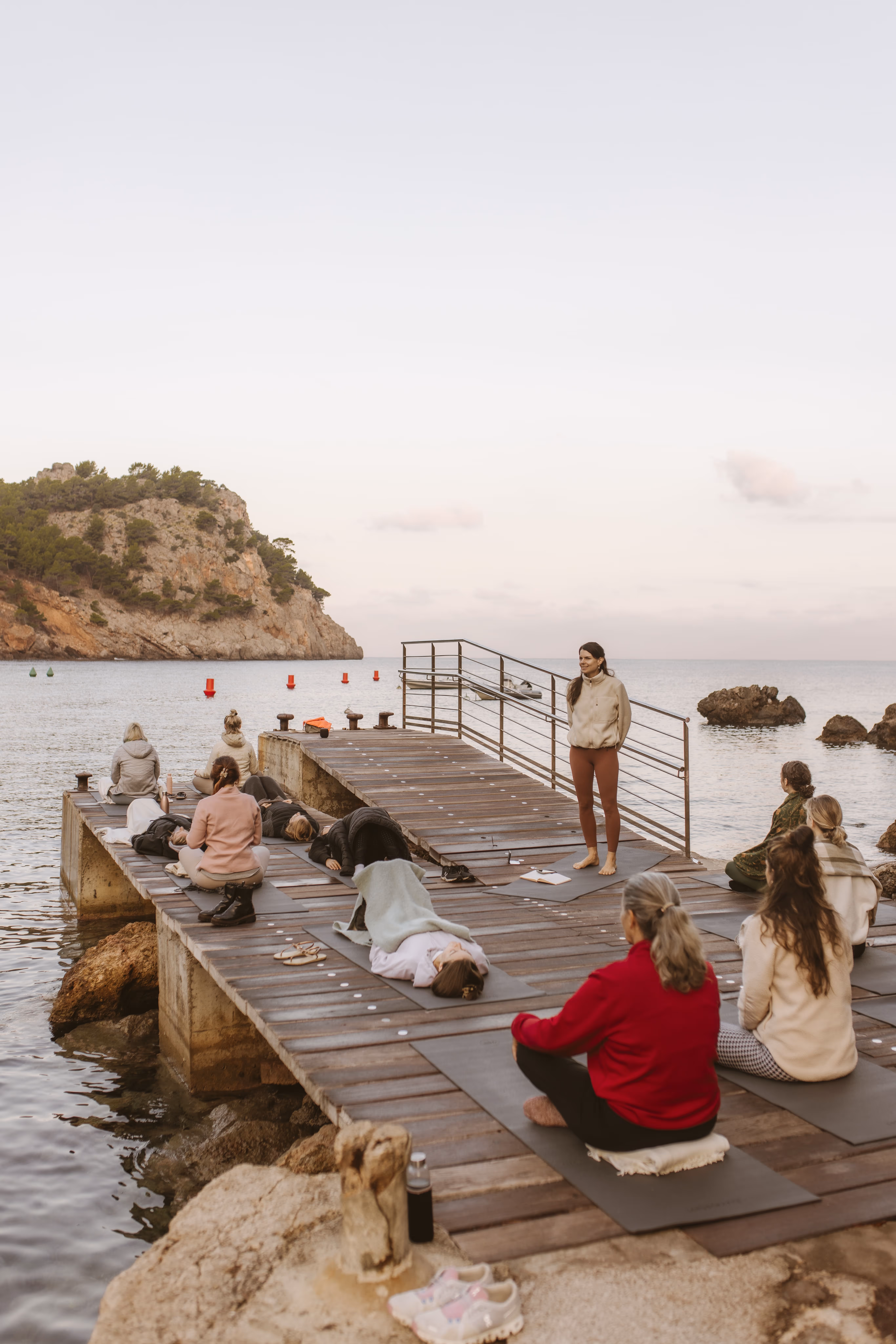 Yoga teacher guiding a meditation session on a pier in Mallorca, with retreat participants practicing at sunset.