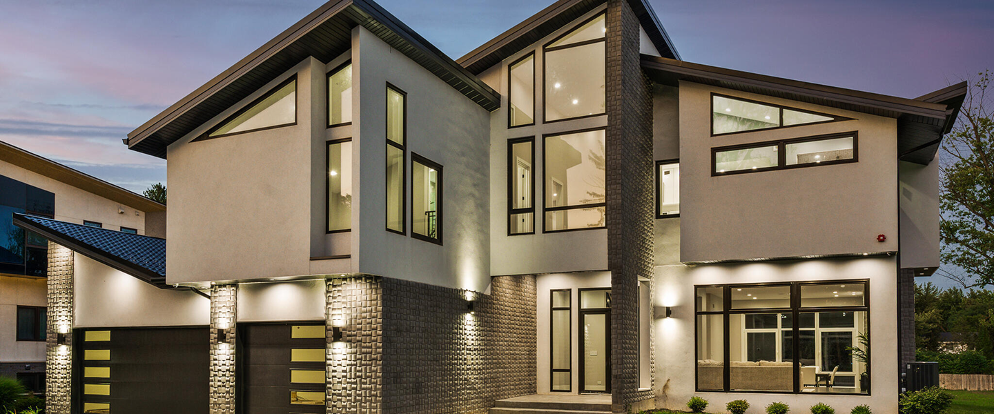 Modern two-story house with large angled windows and exterior lighting at twilight.