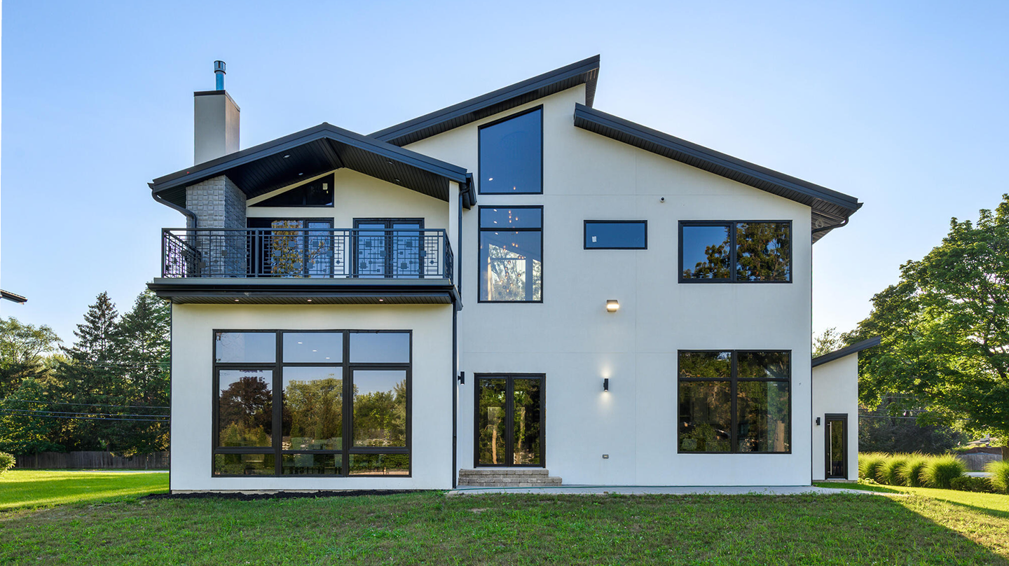 Modern two-story house with large windows, balcony, and a sloped roof on a green lawn.