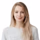 Smiling young woman with long blonde hair wearing a light grey t-shirt against a white background.