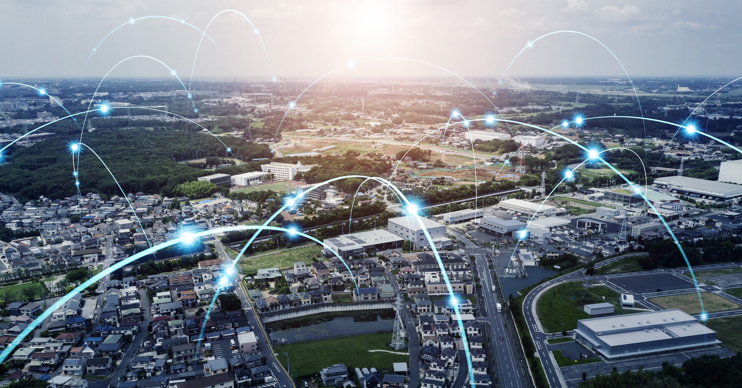 Aerial view of a suburban area with roads, houses, and buildings interconnected by glowing blue digital network lines representing communication and connectivity.