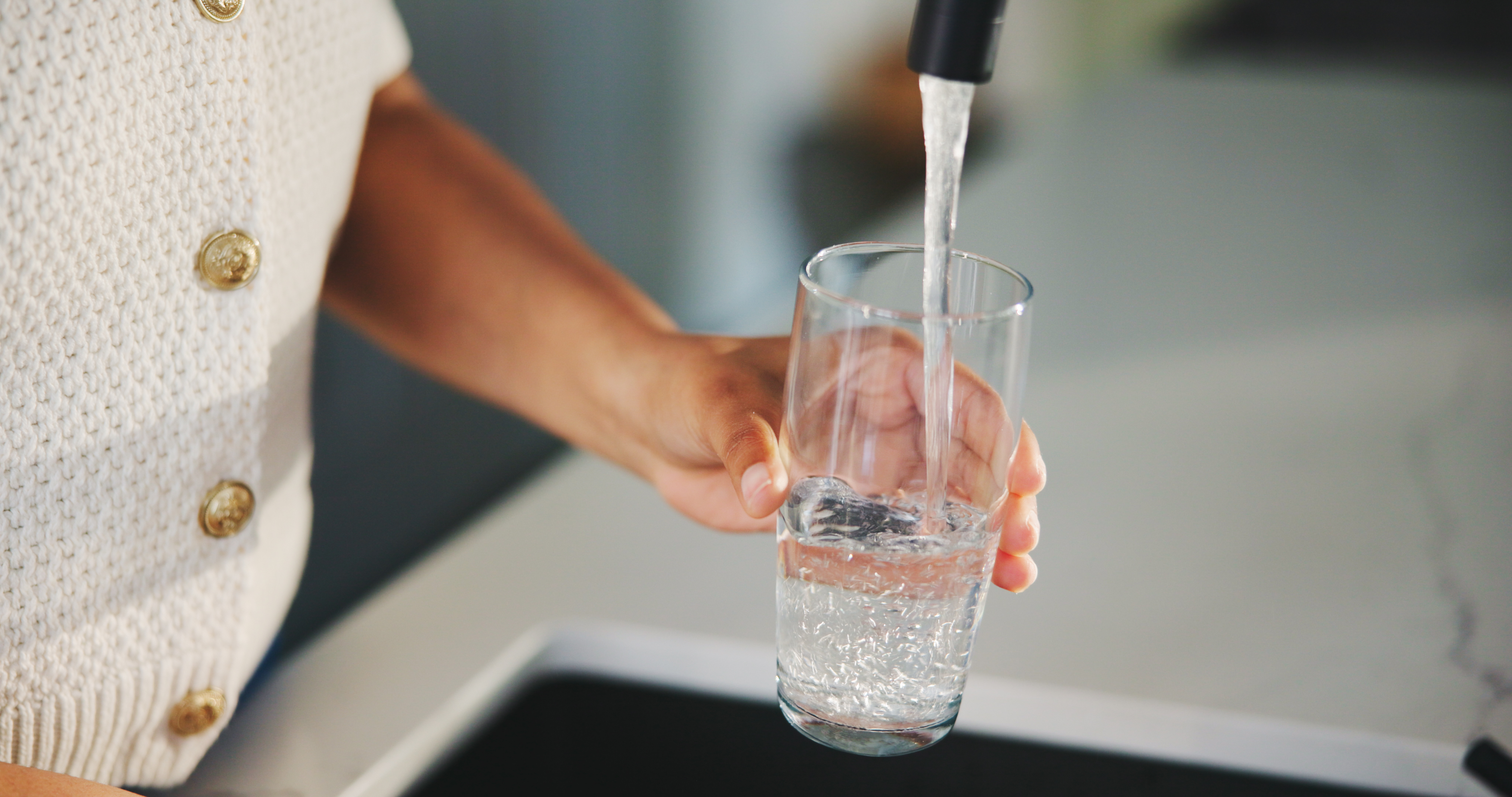 Close-up of a person's hand holding a clear glass while filling it with water from a faucet over a kitchen sink.