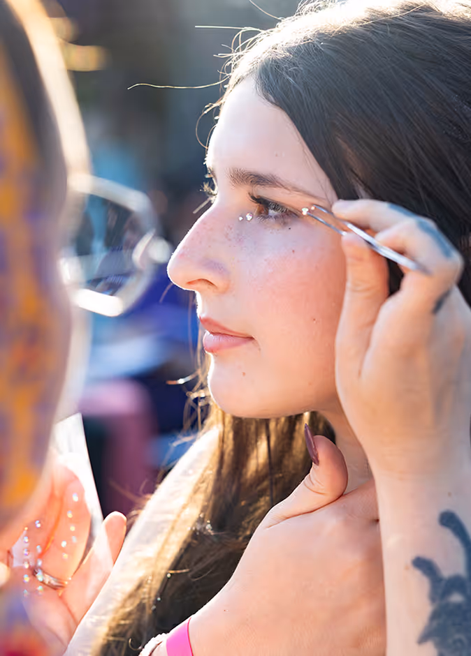 Woman applying small decorative gems near her eye using tweezers in bright sunlight.