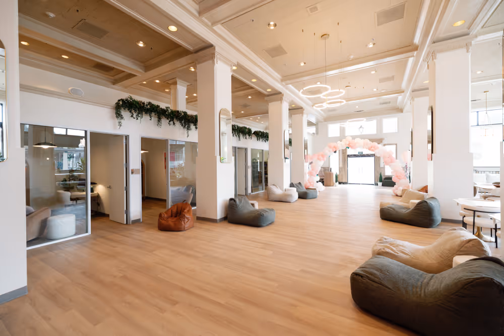 Spacious room with wooden floor, bean bags, white pillars, and pink balloon arch near the entrance.