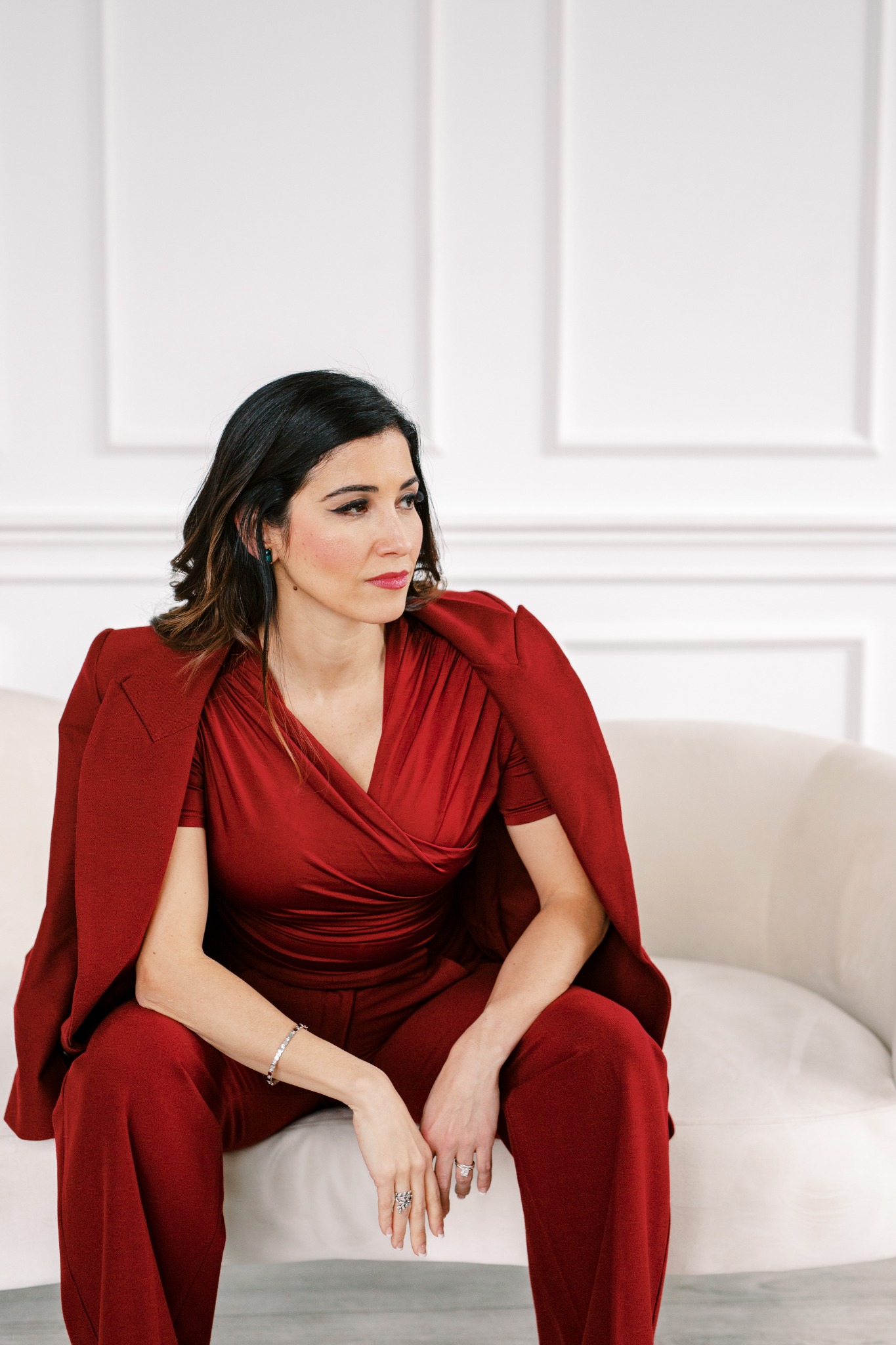 Nayli Russo seated in a red suit, looking to the side.