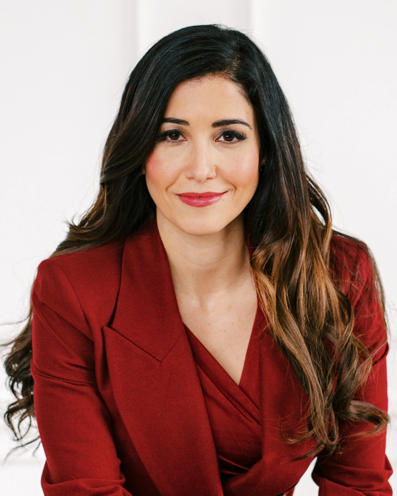 Nayli Russo leaning forward with a slight smile, wearing a red suit.